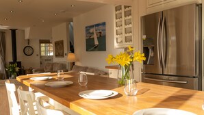 Una cocina moderna con una isla de madera, electrodomésticos de acero inoxidable y un comedor con sillas blancas y un jarrón de flores amarillas.