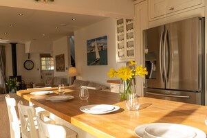 Una cocina moderna con una isla de madera, electrodomésticos de acero inoxidable y un comedor con sillas blancas y un jarrón de flores amarillas.