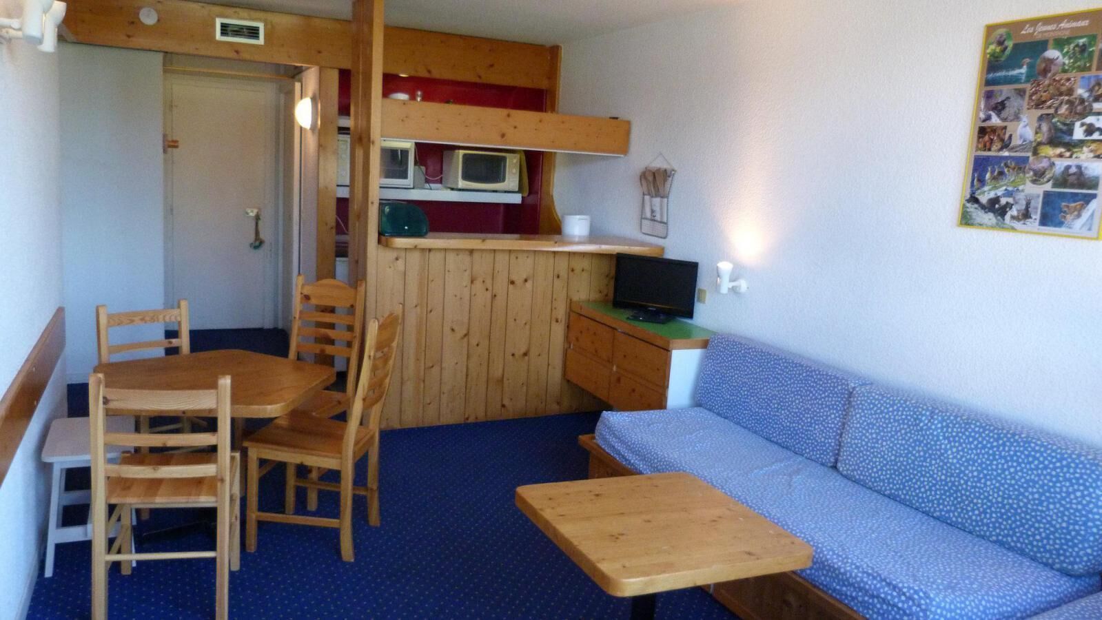 Une pièce de taille modeste comprenant une table et des chaises, un canapé, une petite kitchenette équipée d’un four à micro-ondes et un téléviseur.