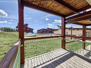 A wooden deck with a metal railing overlooking a grassy area and buildings in the background. - Ski-in/ski-out & foot of the slopes, Ground floor, view resort, tv, 35m², Les Arcs (Les Arcs)