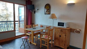 A cozy room with a wooden table and chairs, a TV mounted on the wall, a microwave, and a cabinet. - 100m from ski slopes, 2nd floor, view firs, swimming pool, balcony, tv, 30m², Les Arcs (Les Arcs)