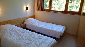A small, simple room with two single beds, a nightstand, and a window with curtains. - 14th floor, view valley, terrace, tv, 54m², Les Arcs (Les Arcs)