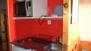 Een kleine keuken met een rode wand, een magnetron, een fornuis en een spoelbak.