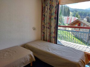 Et lille værelse med to senge, et vindue der viser en balkon og en bygning.