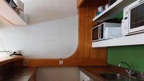 Ett kompakt kök med träskåp, en inbyggd mikrovågsugn, en spis och ett diskho.