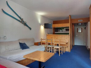 Ein gemütlicher Raum mit einer Sitzecke, einem kleinen Holztisch, einer Essecke mit Stühlen und einem an der Wand befestigten Fernseher.