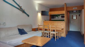 Ett kompakt rum med en soffa, ett litet träbord, en matplats med stolar och en tv som är monterad på väggen.