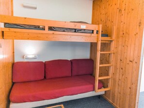 A bunk bed with a red mattress and a wooden ladder.
