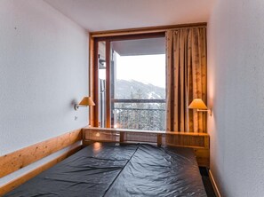 A small room with a wooden headboard, a window with curtains, and a view of snow-capped mountains. - 6th floor, view valley, tv, 40m², Les Arcs (Les Arcs)