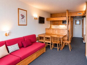 Une pièce avec un canapé rouge, une table à manger en bois, des chaises, un téléviseur et un tableau encadré accroché au mur.