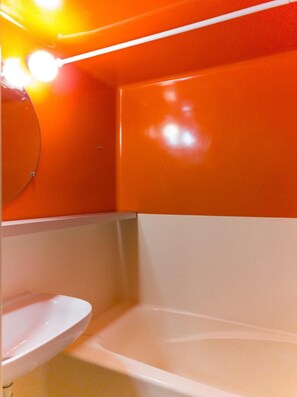 A bathroom with a white sink and bathtub, orange walls, and a mirror. - 6th floor, view valley, tv, 40m², Les Arcs (Les Arcs)
