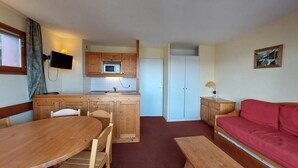 Ett kompakt bostadsutrymme med ett litet kök, en matplats, en soffa och en tv.