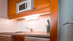 Ett kompakt kök med träskåp, en inbyggd mikrovågsugn, en diskmaskin och ett diskho.