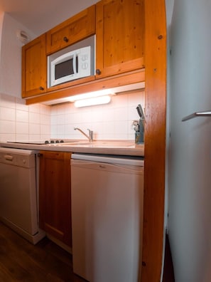 A compact kitchen with wooden cabinets, a built-in microwave, a dishwasher, and a sink.