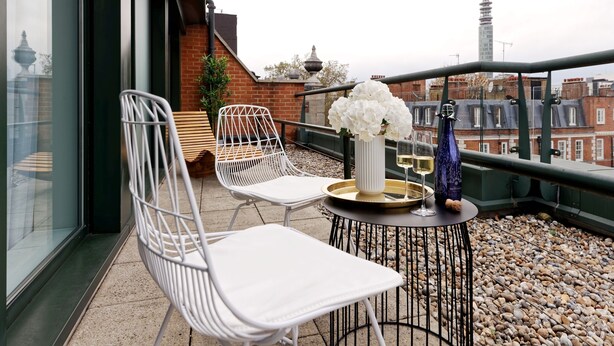 A balcony with white chairs, a small round table with a vase of flowers, and a bottle of champagne. - Fitzrovia apartments by DMONTRIO (London)