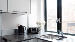 A modern kitchen with a black toaster, a kettle, and a vase with white flowers on the counter. - Fitzrovia apartments by DMONTRIO (London)
