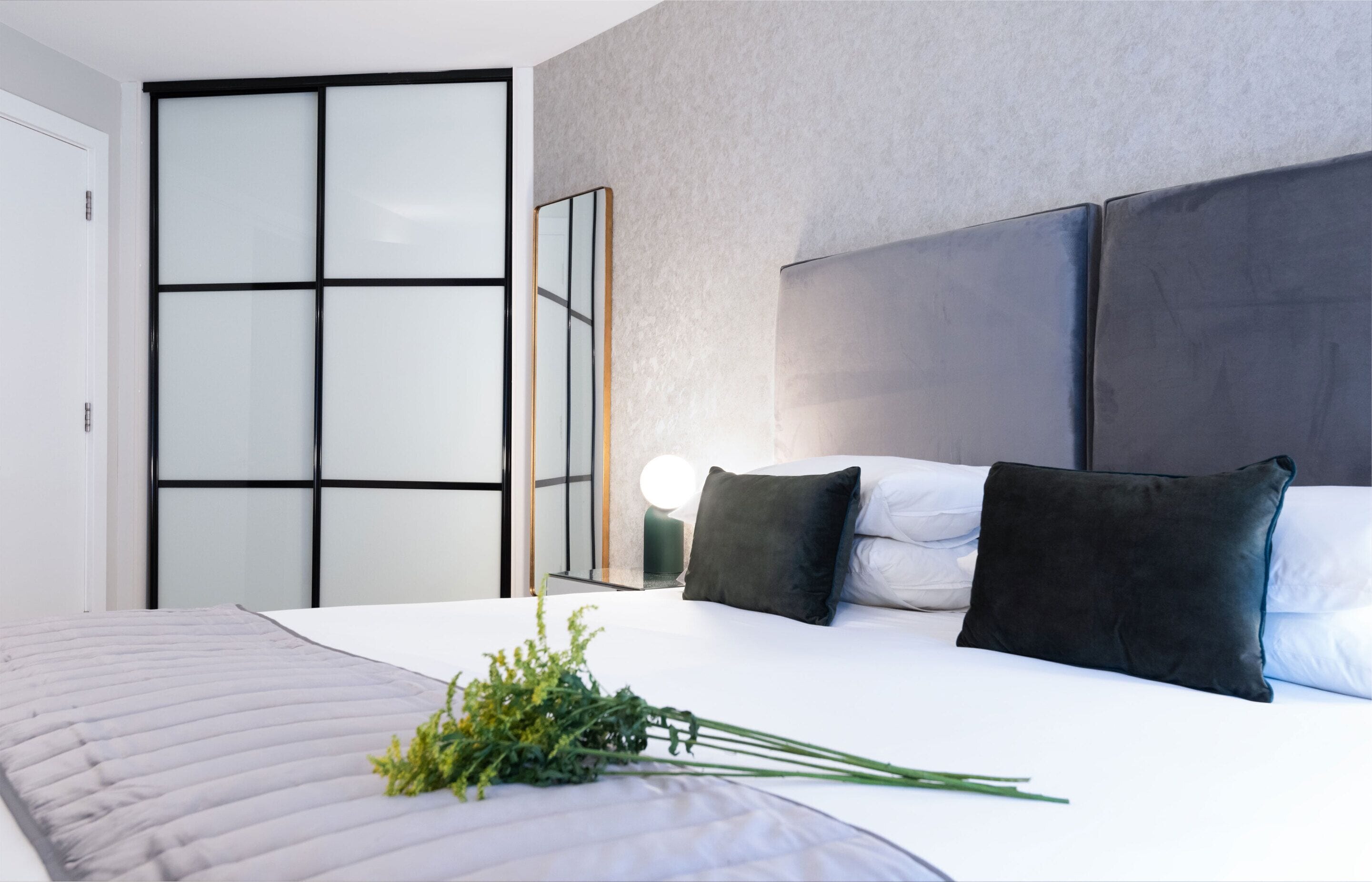 A modern bedroom with a large bed, a mirror, and a sliding door.