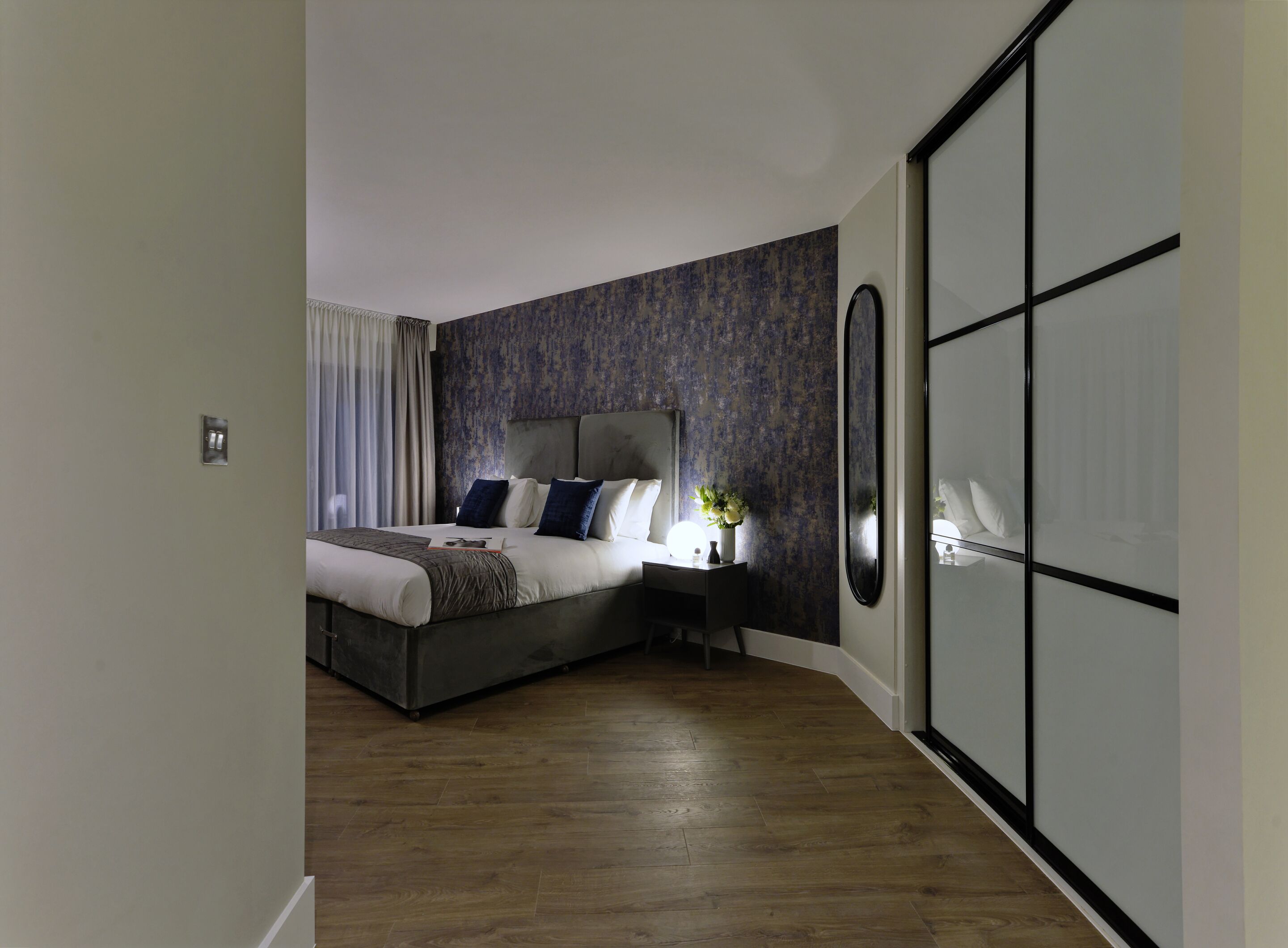 A modern bedroom with a large bed, a nightstand, a mirror, and a wardrobe.