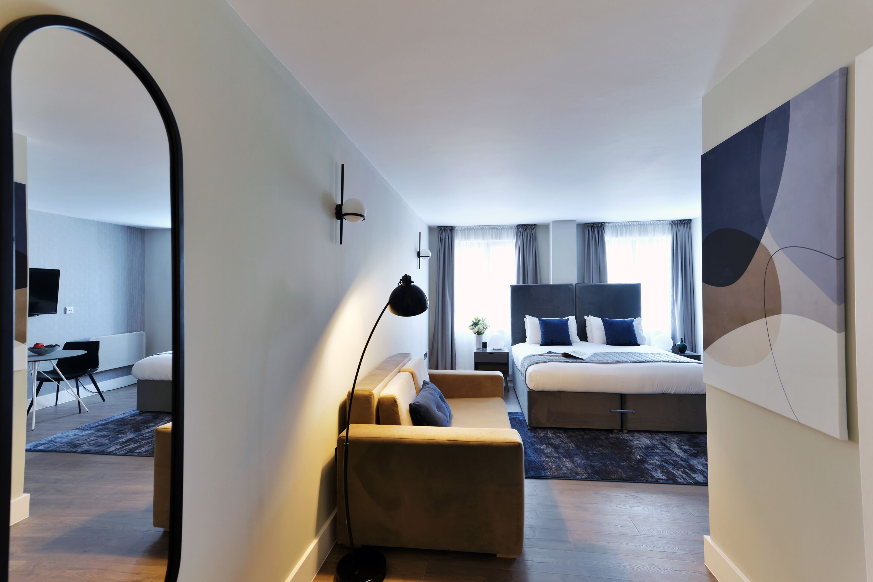 A modern hotel room with a bed, a sofa, a desk, and a dining area.