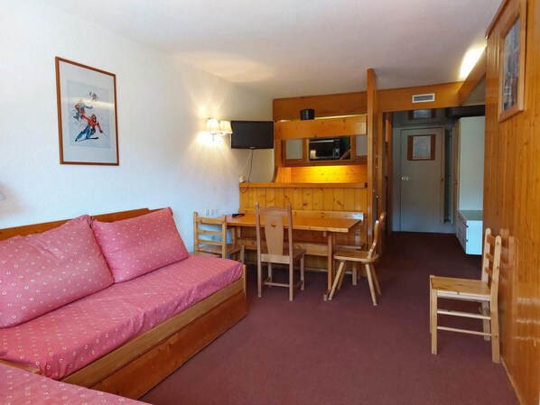 Una habitación acogedora con un sofá de madera, una mesa de comedor con sillas, un televisor y una kitchenette.