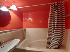 Un baño con una bañera blanca, un espejo redondo y una cortina de ducha a rayas.