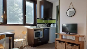 A compact kitchen with a microwave, oven, and sink, a dining area with a table and chairs, a television on a wooden stand, and a large window with a view of trees. - 8th floor, view firs, tv, 13m², Les Arcs (Les Arcs)