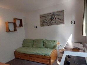 Ein kleiner, gemütlicher Raum mit einem hölzernen Bett, einem grünen Kissen, einem Gemälde an der Wand und einem kleinen Tisch mit einer Lampe.