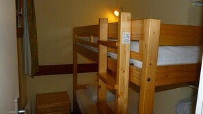 A bunk bed with a wooden frame, a small wooden chest, and a wall-mounted shelf.