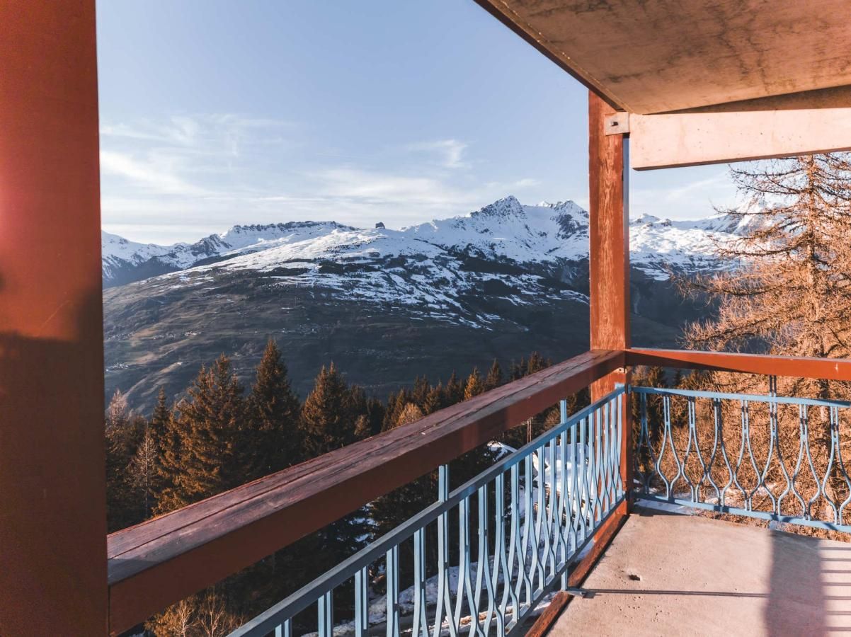 A balcony with a metal railing overlooking a mountainous landscape with snow-capped peaks.