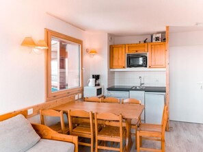 A compact kitchen with wooden cabinets, a microwave, a sink, and a dining area with a table and chairs.