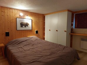 A bedroom with a wooden paneled wall, a framed picture, a bed with a brown blanket, a wardrobe, and a shelf with a red patterned item. - 300m from ski slopes, 4th floor, view valley, tv, 65m², Les Arcs (Les Arcs)