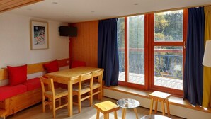 A cozy room with a wooden ceiling, a wooden dining table with chairs, a sofa with red cushions, a small stool, and a TV on the wall. - 300m from ski slopes, 4th floor, view valley, tv, 65m², Les Arcs (Les Arcs)