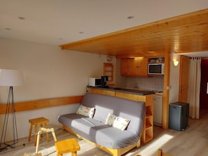Un espace de vie compact comprenant un canapé, une petite table, une lampe, un coin cuisine et un téléviseur.