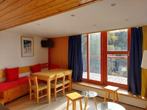 A cozy room with a wooden ceiling, a wooden dining table with chairs, a sofa with red cushions, a small stool, and a TV on the wall. - 300m from ski slopes, 4th floor, view valley, tv, 65m², Les Arcs (Les Arcs)