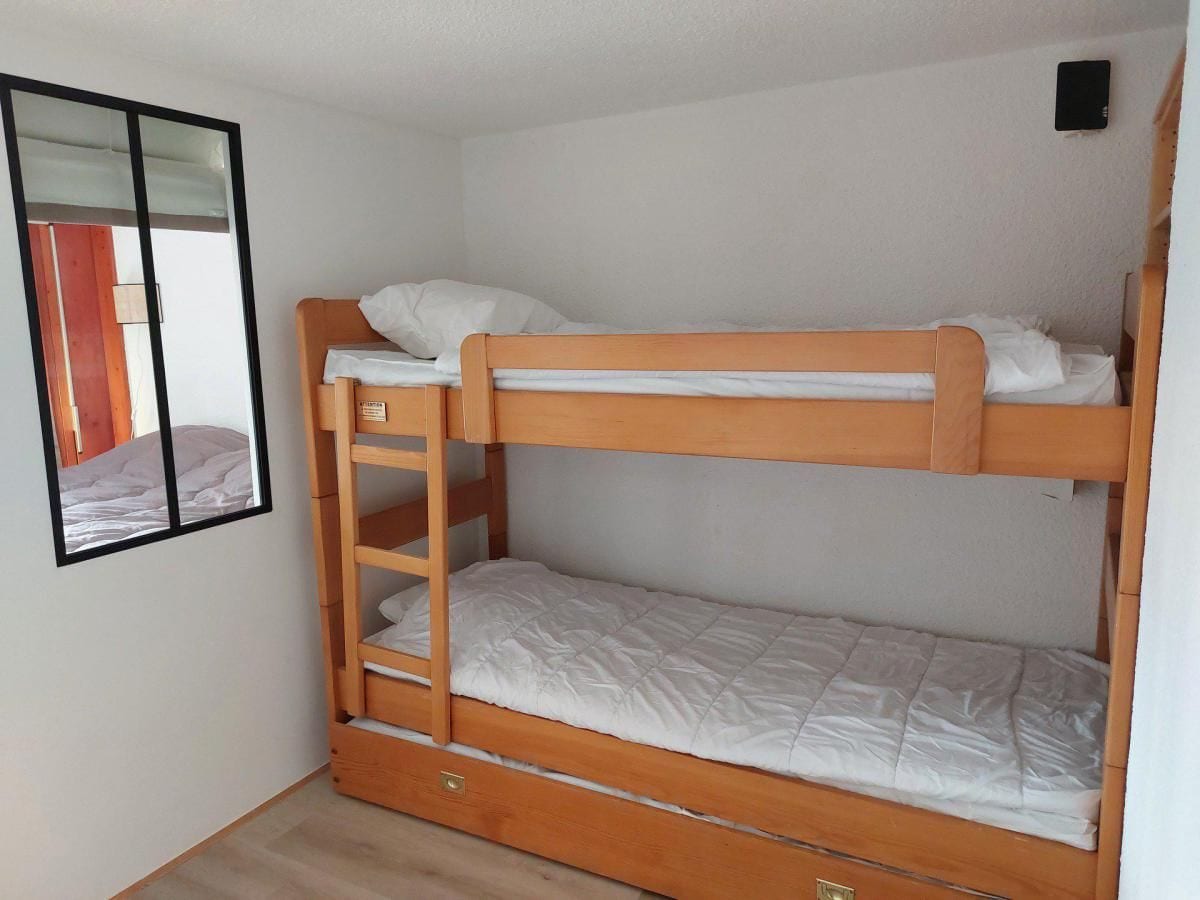 Een stapelbed met een ladder, een klein ladeblok en een spiegel aan de muur.