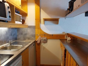 A compact kitchen with a sink, stove, microwave, and wooden cabinets.
