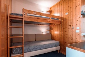 A bunk bed with a ladder, a small desk, and a wall-mounted shelf.