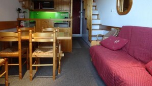 Une pièce de taille modeste comprenant une table et des chaises, un coin cuisine, un canapé et un escalier.