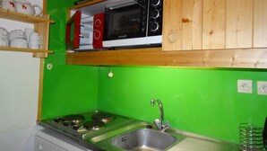 Une cuisine de taille réduite, équipée d’une cuisinière à gaz, d’un évier, d’un four à micro-ondes et de meubles de rangement en bois.