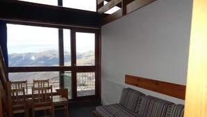 Una habitación con una mesa de madera, sillas, un sofá a rayas y un ventanal con vistas a montañas.