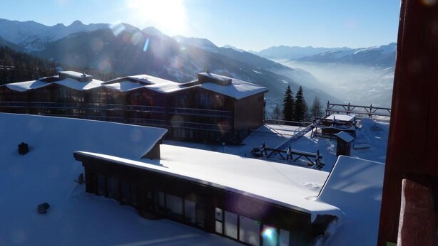 Un edificio cubierto de nieve con un amplio ventanal, rodeado de montañas y un cielo despejado.