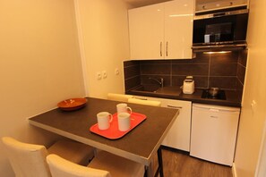 Kompakti keittiö, jossa on ruokapöytä, tuolit, punainen tarjotinalusta, mikroaaltouuni, pesuallas ja astianpesukone.