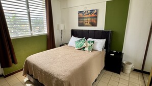 Une chambre d’hôtel bien rangée, avec un lit, une table de chevet, une lampe, un tableau au mur et une vue sur l’extérieur par la fenêtre.