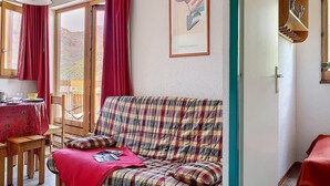 Una sala de estar acogedora con un sofá de cuadros, una mesa de comedor con sillas y un ventanal con cortinas rojas.