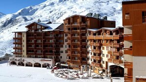 Un hotel de varios pisos con balcones y una montaña nevada al fondo.