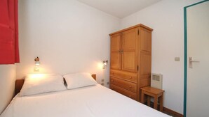 Un dormitorio con cama, lámparas de noche, un armario de madera y una mesita.