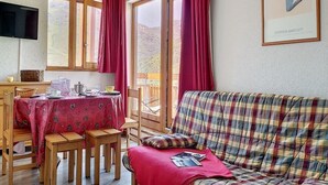 Una habitación acogedora con una mesa de comedor para dos personas, un sofá escocés y un amplio ventanal con cortinas.