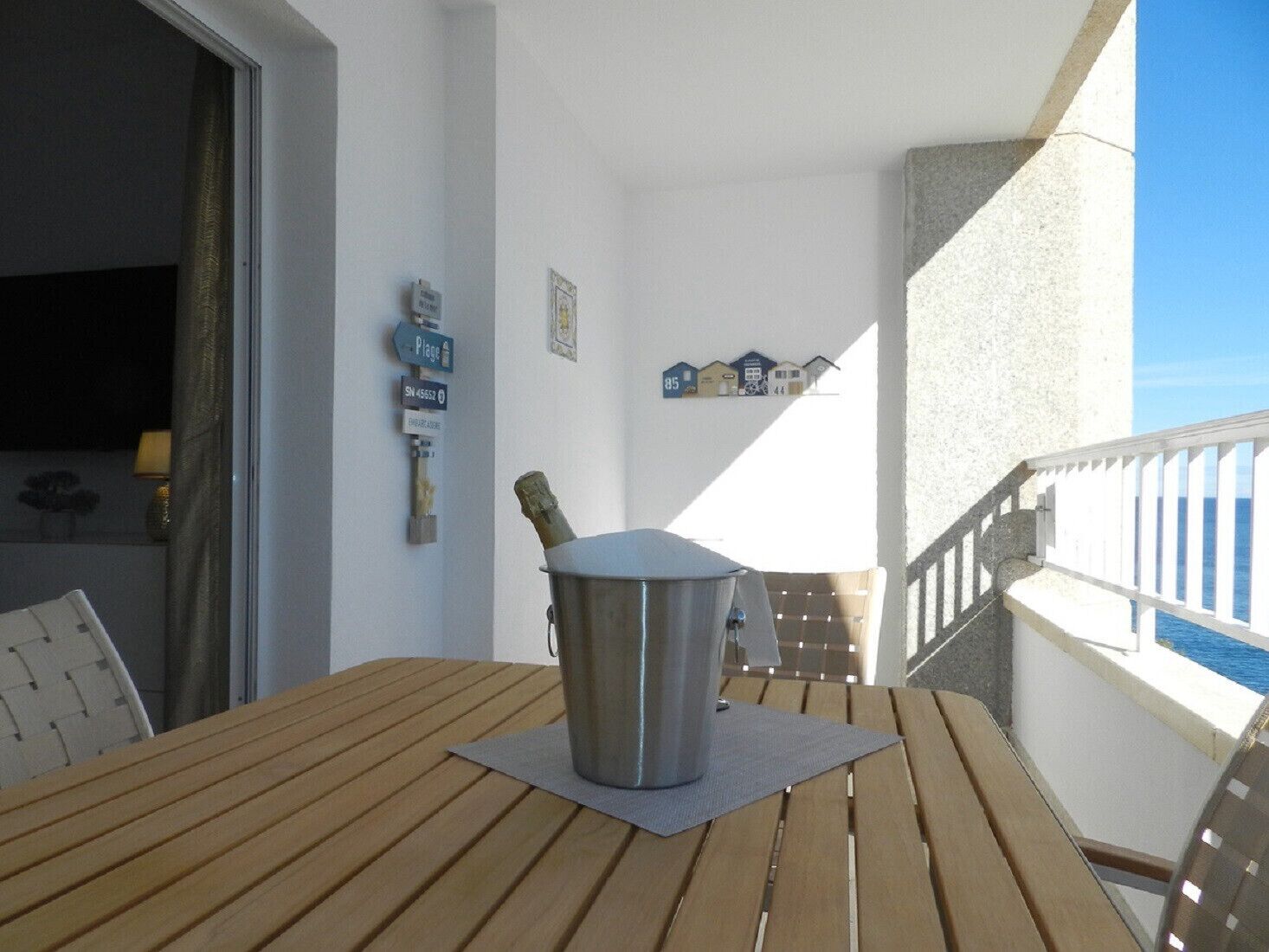 A wooden table with a metal container on a balcony with a railing and a view of the sea.
