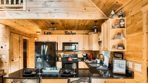 A wooden cabin kitchen with a central island, a refrigerator, stove, microwave, and a coffee maker. - Pet Friendly Cabin|Hot Tub|Pool Table|Outdoor Fireplace (Blue Ridge)