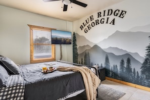 A bedroom with a bed, a window with blinds, a wall mural, and a ceiling fan.